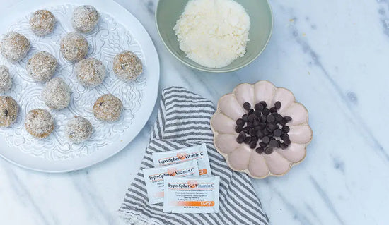 almond bites with chocolate chips on a marble counter with bowl of shredded coconuts, chocolate chips, and lypo c packets